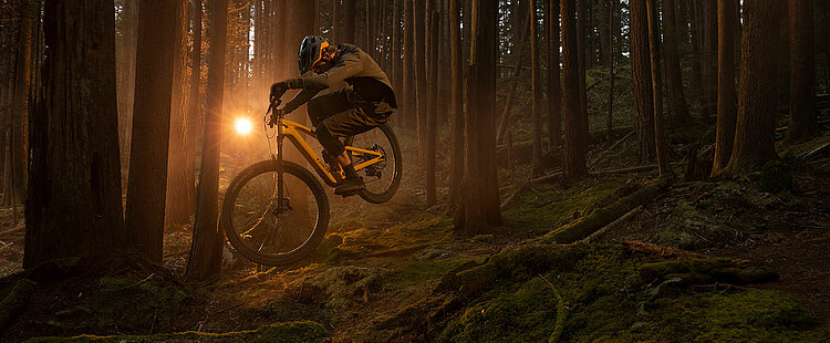 Biker springt bei Abenddämmerung mit Trek Fuel EXe E-Bike im Wald